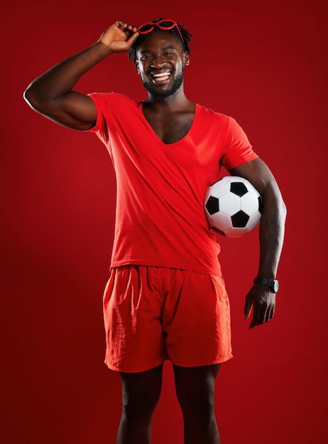 Foto bola de futebol de homem negro e futebol em estúdio com felicidade e roupas vermelhas com óculos escuros e uma mentalidade positiva para esportes retrato de um homem da frança feliz e rindo na moda de verão