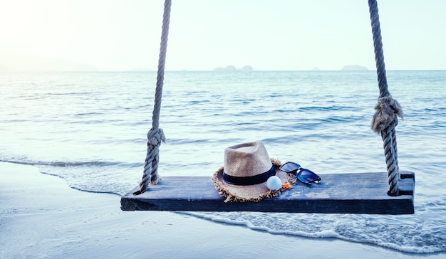 Bola de golfe do chapéu e óculos no balanço na praia de areia com o mar ao fundo.