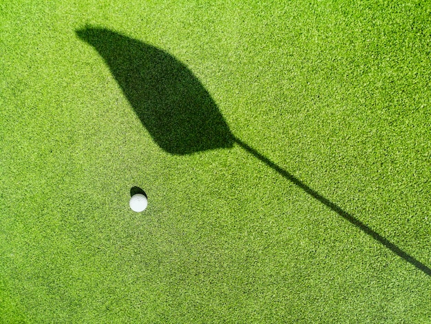 Bola de golfe no gramado, sombra de uma bandeira no gramado, campo de golfe