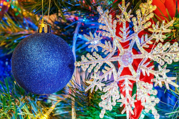 Bola de natal azul contra um floco de neve de vidro e guirlanda de cor luminosa