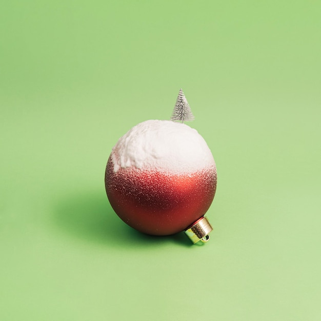 Bola de natal decorada com uma árvore de natal na neve contra um fundo verde conceito mínimo