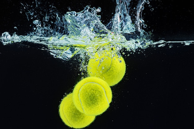 Bola de tênis caindo na água com um respingo contra um fundo preto escuro