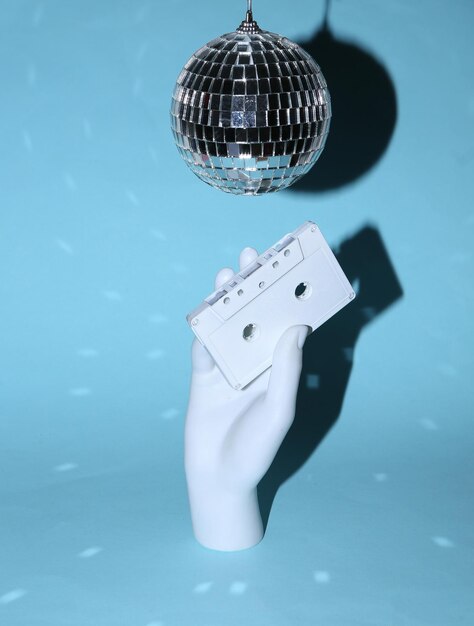 Bola de discoteca y mano con casete de audio sobre fondo azul brillante Concepto de fiesta minimalista