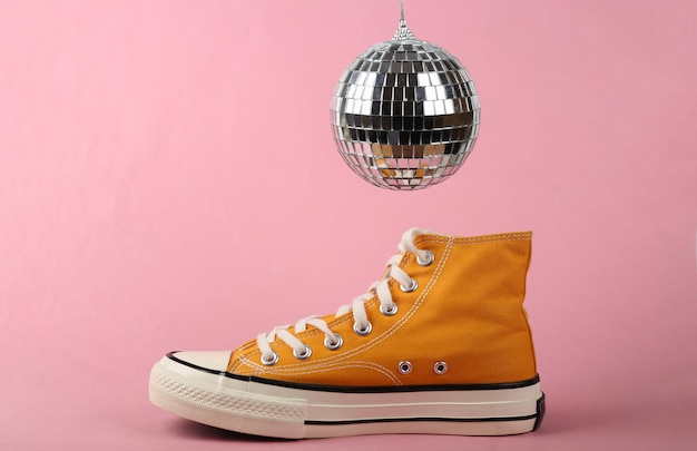 Bola de discoteca y zapatillas sobre fondo rosa Concepto de fiesta minimalista