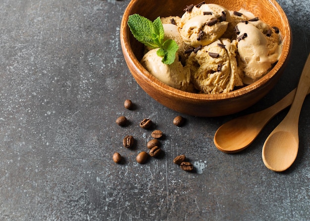 Bola de helado de café o chocolate en placa de madera con hoja de menta sobre fondo oscuro