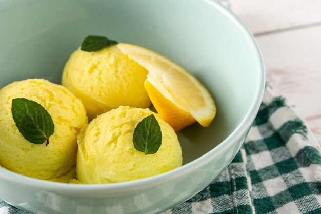 Bola de helado de limón decorada con hojas de menta en la mesa de madera blanca
