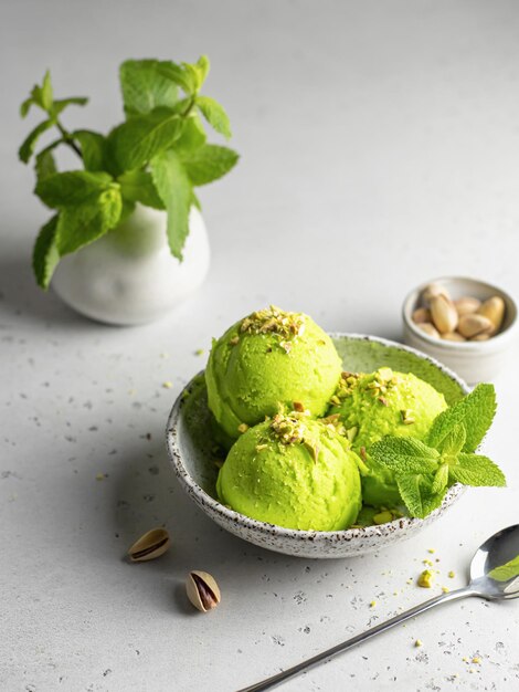 Bola de helado de pistacho adornada con pistachos picados y menta con cuchara de plata sobre fondo de textura gris