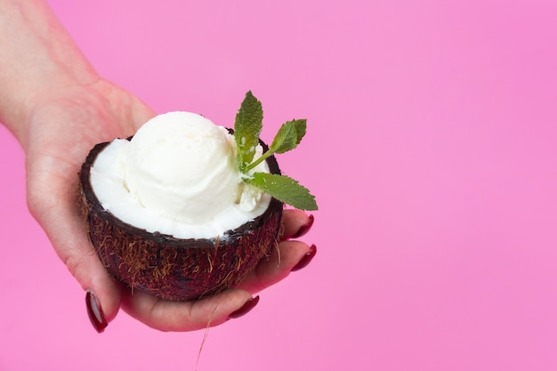 Bola de helado de vainilla en mitad de coco fresco decorado con hojas de menta sobre un fondo rosa