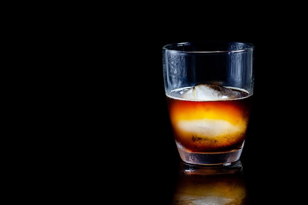 Bola de hielo en vaso de whisky sobre una mesa negra reflectante.