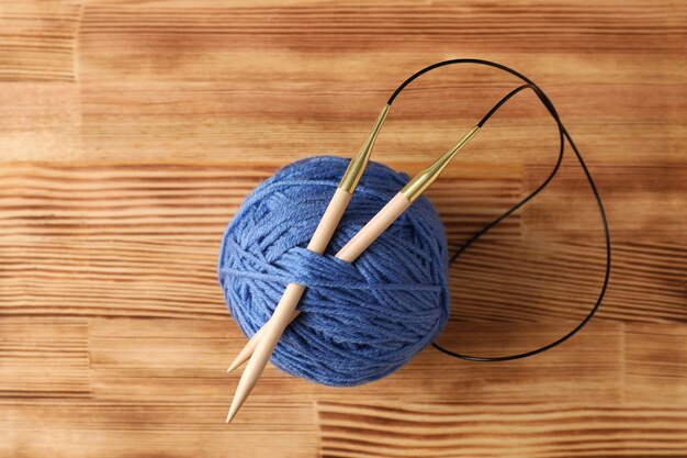 Bola de hilo azul con agujas de tejer sobre una mesa de madera clara.