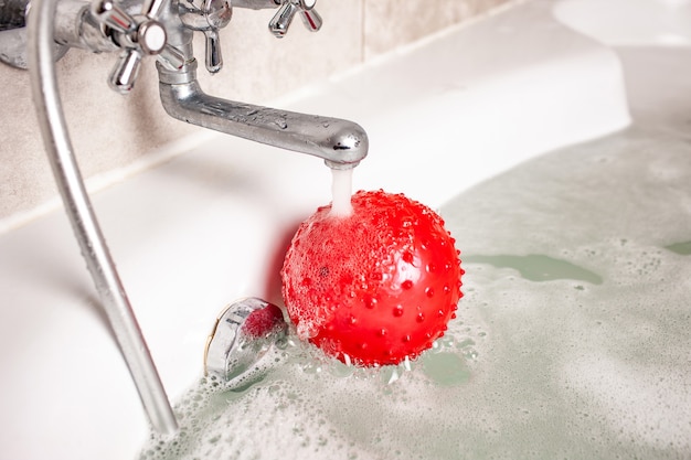 Bola inflable roja para niños se encuentra bajo un chorro de agua en el baño de espuma