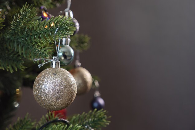 Bola de juguete decorativa de navidad de plata cuelga de la rama de un árbol verde artificial contra la guirnalda borrosa vista de cerca extrema