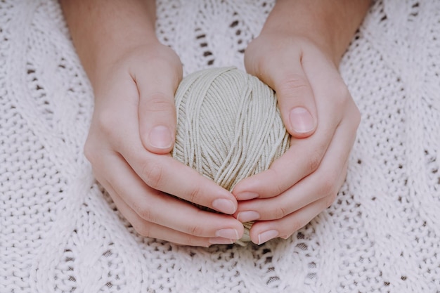 Bola marrom de lã nas mãos no fundo de uma toalha de mesa de malha branca. foto de alta qualidade