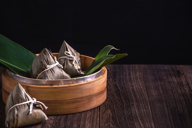 Bola de masa hervida de arroz chino Zongzi zongzi en un vapor sobre una mesa de madera fondo retro negro para la celebración del Festival del Bote del Dragón cerca del espacio de copia