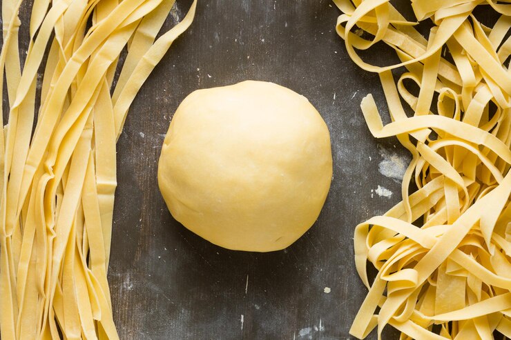 Foto bola de masa y rayas crudas rectas y curvas de fideos sobre fondo de madera