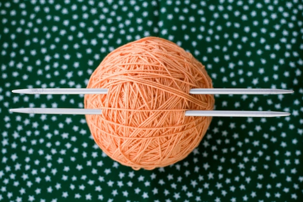 Una bola naranja brillante de hilo y agujas para tejer sobre un fondo verde