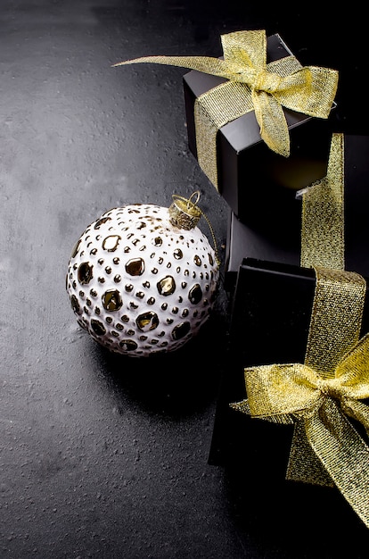 Bola de Navidad y caja de regalo negra con cinta dorada sobre fondo negro.