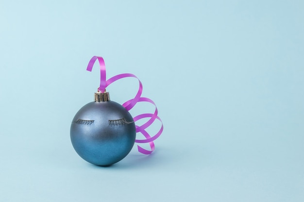Bola de Navidad con pestañas y cinta rosa sobre fondo azul. El concepto mínimo del Año Nuevo. Una fiesta.