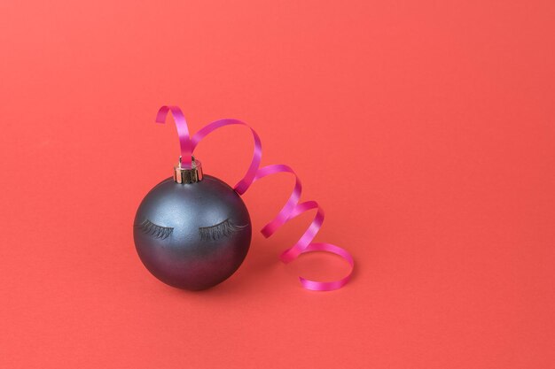 Una bola de Navidad con pestañas y una serpentina sobre un fondo rojo. El concepto mínimo del Año Nuevo.