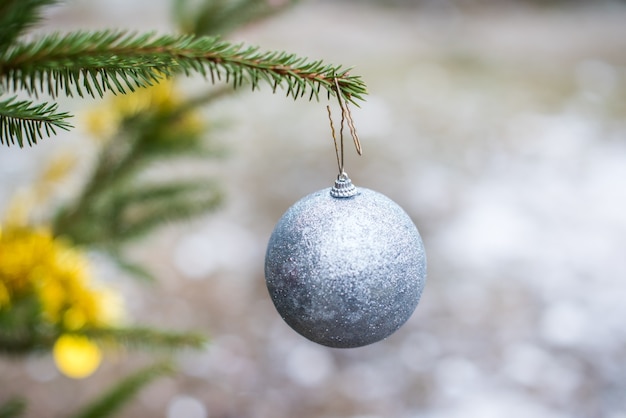 Bola de Navidad con purpurina plateada colgando de un árbol de hoja perenne