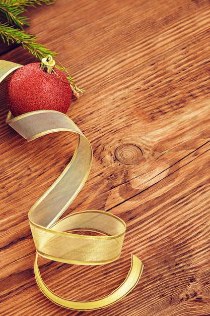 Bola de Navidad roja y cinta dorada en medio de la rama de un árbol de Navidad Fondo de madera