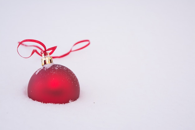 Bola de Navidad roja con una cinta roja sobre nieve blanca esponjosa.