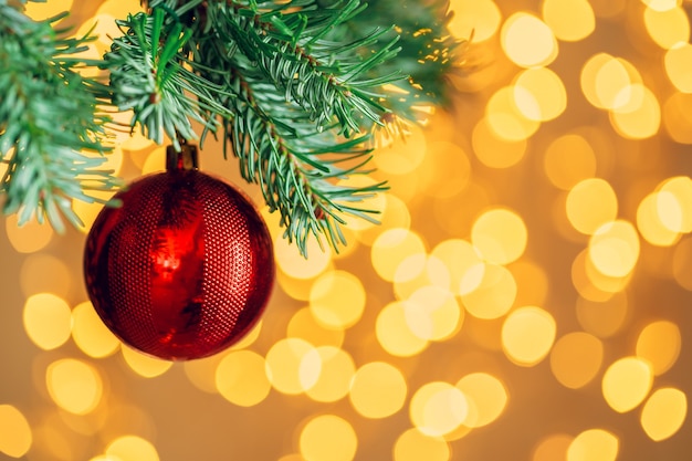 Bola de Navidad roja colgando de la rama de un árbol de abeto sobre fondo dorado de luces bokeh