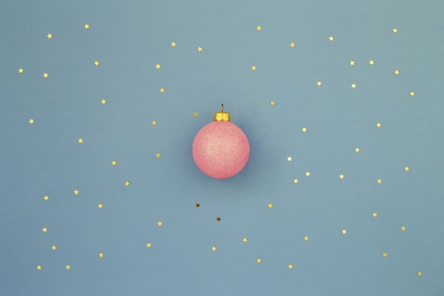 Bola de Navidad rosa sobre fondo azul con confeti de estrellas doradas