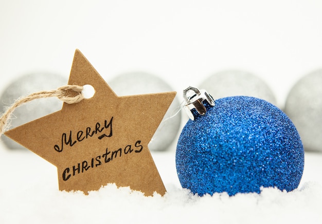 Bola navideña en azul sobre nieve blanca y una estrella con la inscripción Feliz Navidad