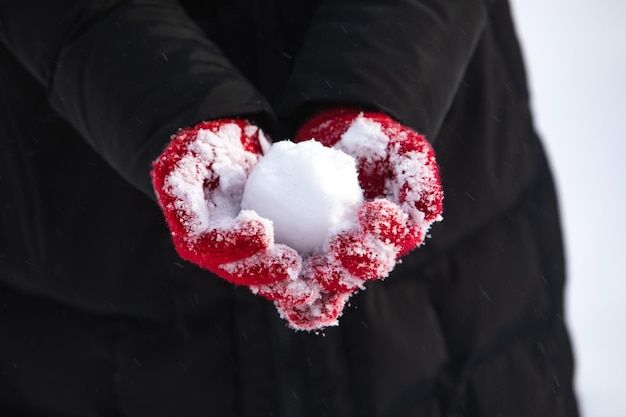 Bola de nieve sin cara en manos de mujer con guantes rojos