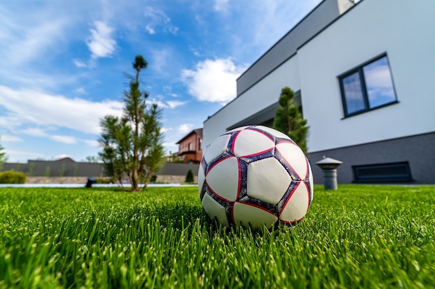 Foto bola no gramado verde. fundo moderno da casa desatualizada. céu azul acima. ninguém no quintal. arquitetura moderna.