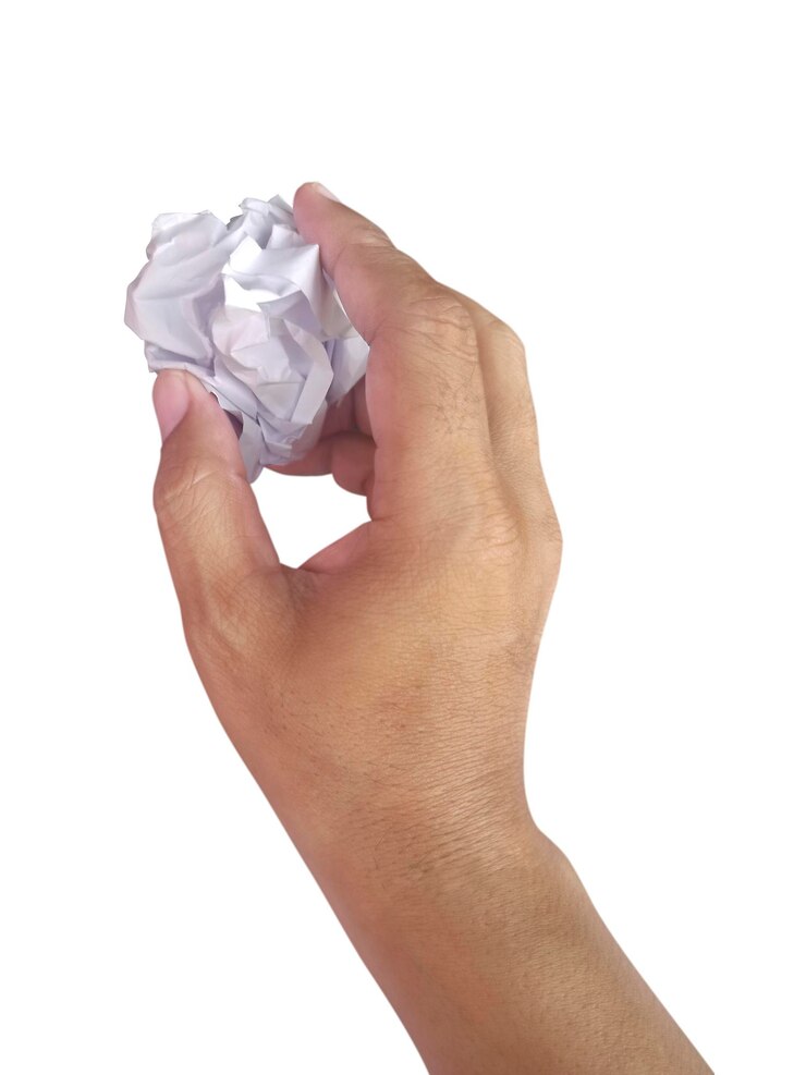 Foto bola de papel en la mano con papel basura arrugado sobre un fondo blanco.