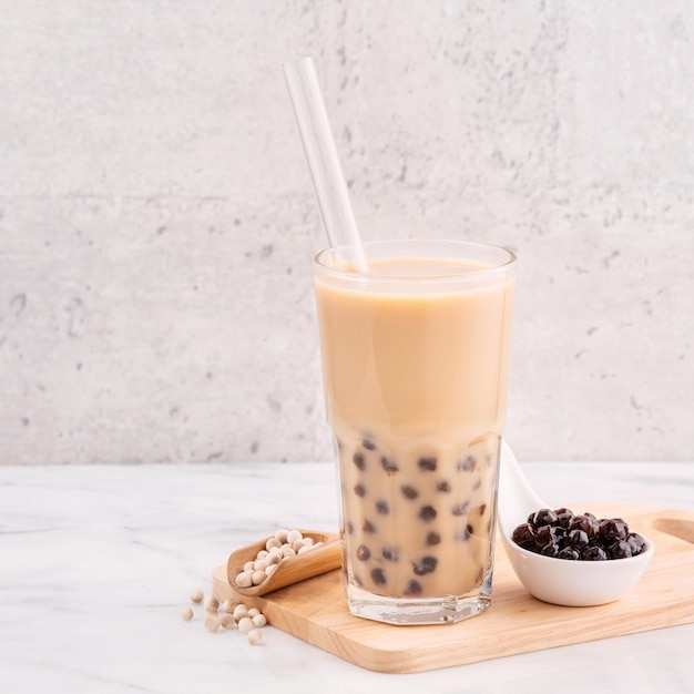 Bola de perla de tapioca, té de leche con burbujas, bebida popular de Taiwán en un vaso con paja sobre una mesa de mármol blanco y una bandeja de madera, cerca del espacio de copia