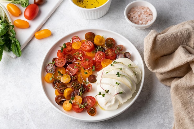 Bola de queso mozzarella con tomates cherry en rodajas sobre un plato blanco con verduras, ensalada caprese.