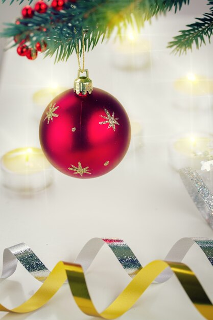 Bola roja de Navidad colgando de abeto azul y luces de velas de fondo desenfocado, tonos retro