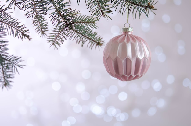 Una bola rosa cuelga de la rama de un árbol de Navidad