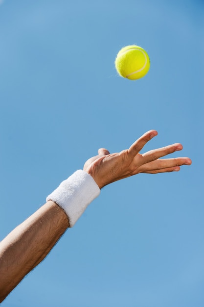 Bola de servicio. Close-up de mano masculina en la pulsera lanzando una pelota de tenis contra el cielo azul