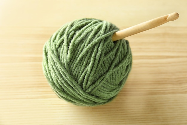 Bola verde de hilo de tejer y gancho en mesa de madera
