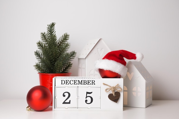 Bola vermelha de Natal com chapéu de Papai Noel no calendário com sacos de presentes datados de 25 de dezembro e árvore de Natal