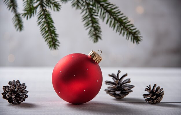 Bola vermelha de Natal e cones em uma mesa de madeira clara e a árvore de Natal fecham. Copie o espaço