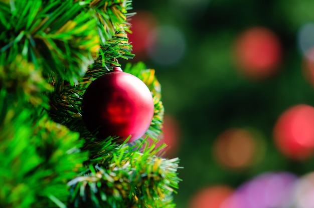 Foto bola vermelha pendurada na árvore de natal com fundo bokeh de outra árvore de natal maior