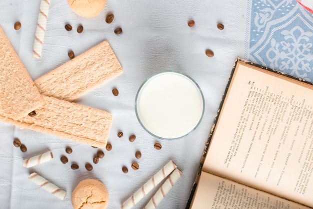 Bolacha de pão e biscoitos com um copo de leite e um livro à parte