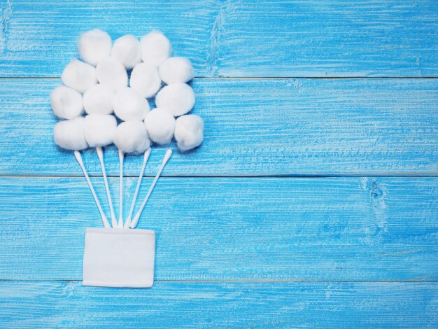 Bolas de algodón absorbente blanco y bastoncillos de algodón en madera azul.