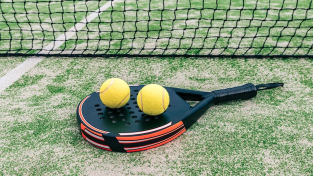 Bolas amarelas sobre a raquete de tênis padel atrás da rede na quadra verde ao ar livre