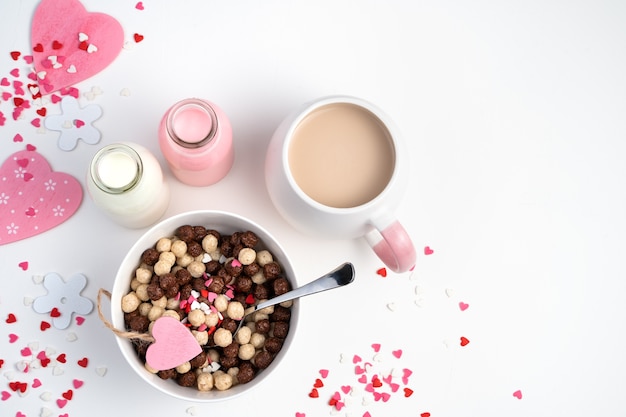 Bolas de cereal de chocolate en un tazón blanco y una taza de café con leche sobre un fondo romántico. Concepto de día de San Valentín