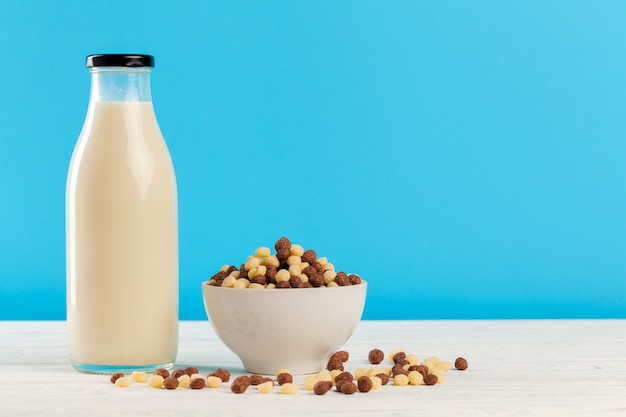 Bolas de cereales para el desayuno y leche en vidrio contra el fondo azul.