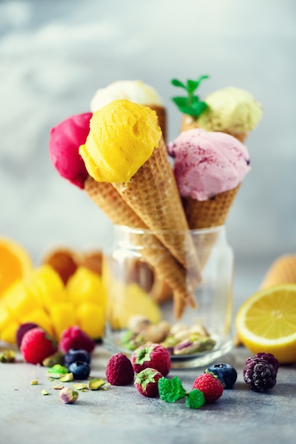 Bolas coloridas do gelado nos cones do waffle com sabores diferentes - manga, cal, hortelã, pistache, laranja, morangos, framboesas, mirtilos. Conceito de verão