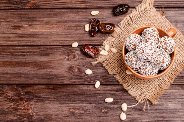 Bolas de dátiles energéticos, nueces, avena, espolvoreadas con primer plano de coco en polvo sobre una mesa de madera