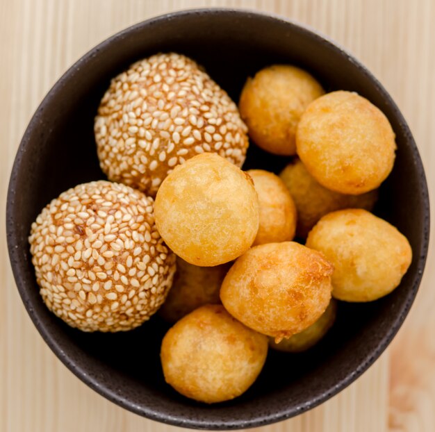 Bolas de batata doce frita em uma tigela preta na mesa de madeira