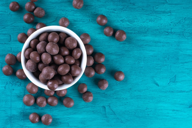 Bolas de chocolate em uma tigela branca na superfície azul.